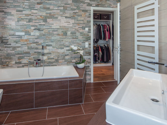 Im Bad von Haus Fuchs werden unterschiedliche Wand- und Bodenfliesen mit einer Natursteinwand kombiniert. (Foto: BAUMEISTER-HAUS)